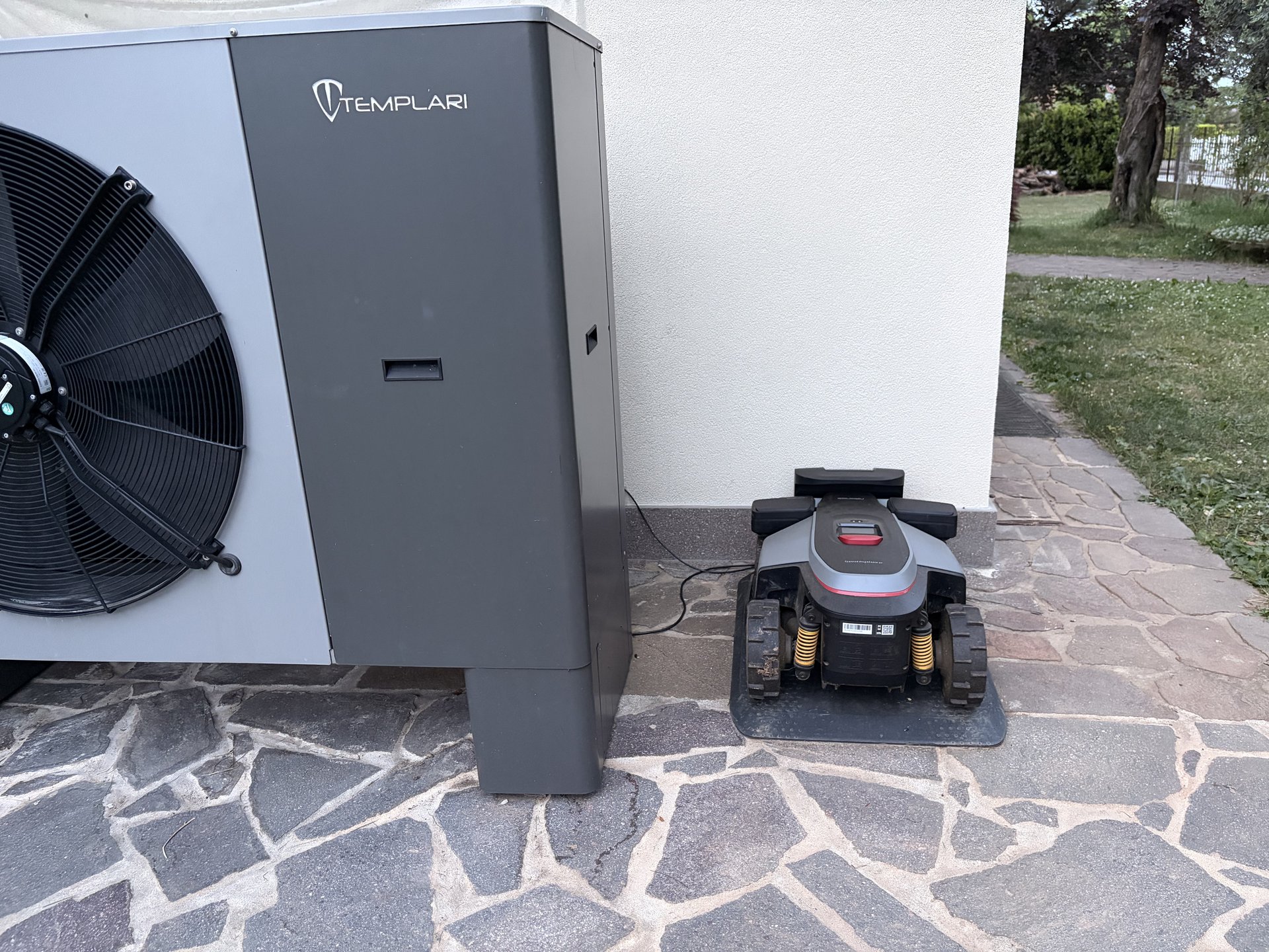 Roborock RockMow Z1 in zona di servizio davanti alla pompa di calore Templari, su pavimentazione in pietra