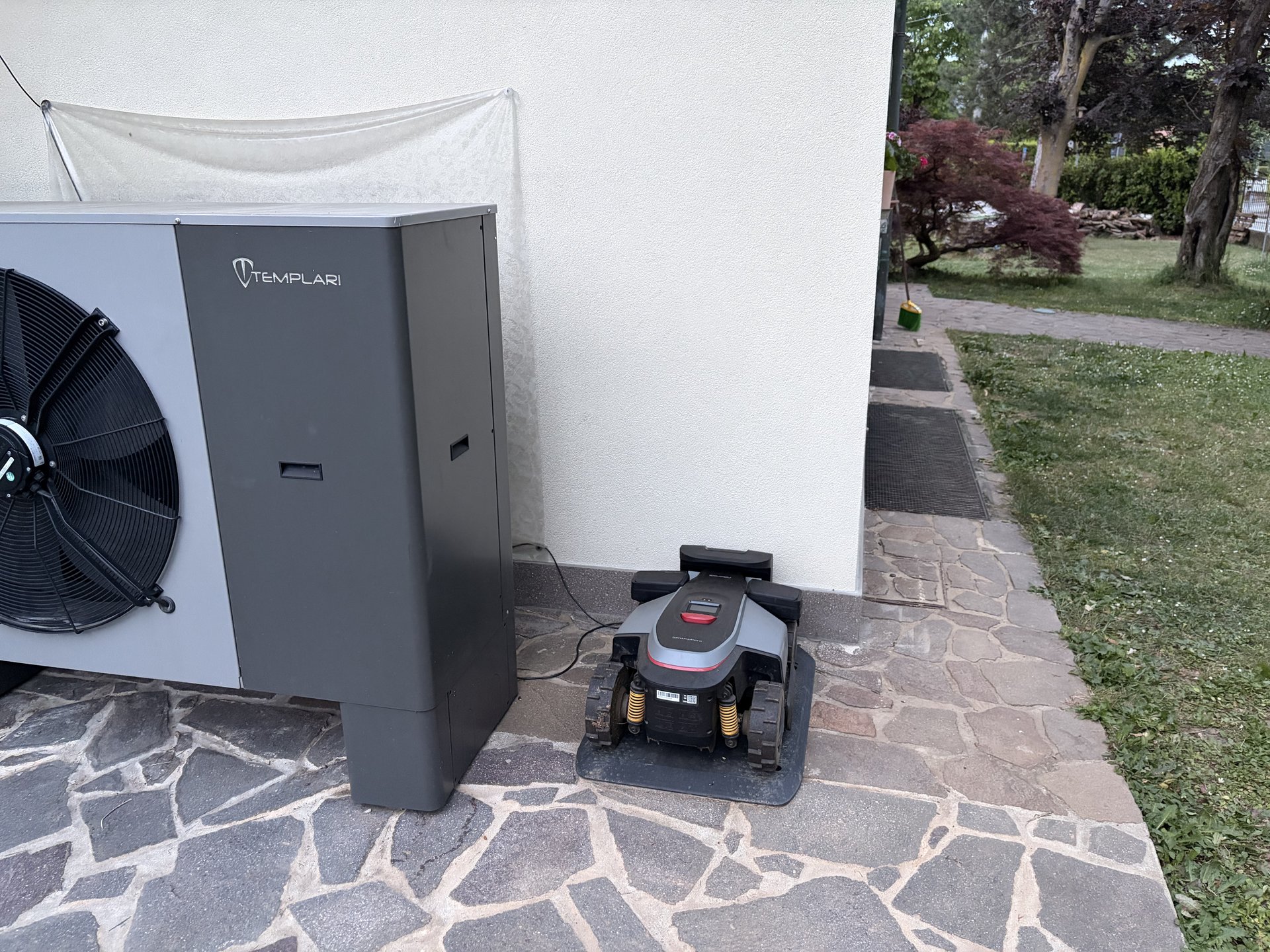 Roborock RockMow Z1 in transito vicino alla pompa di calore Templari su passaggio in pietra del giardino