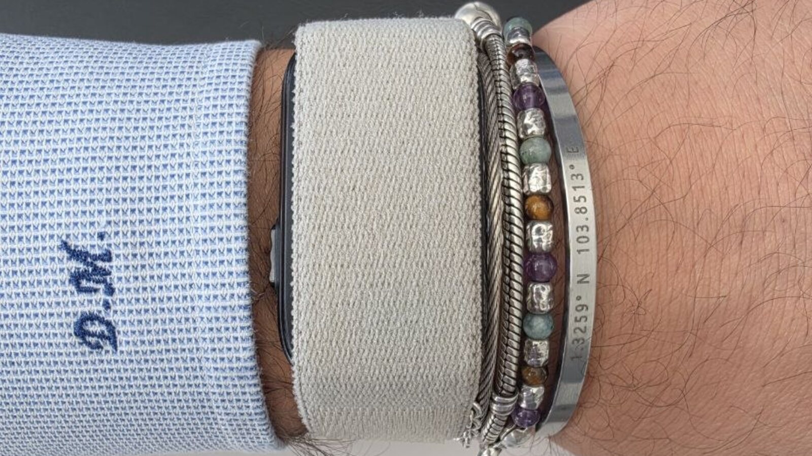Garmin Cirqa con cinturino in tessuto grigio chiaro al polso, accanto ad alcuni bracciali