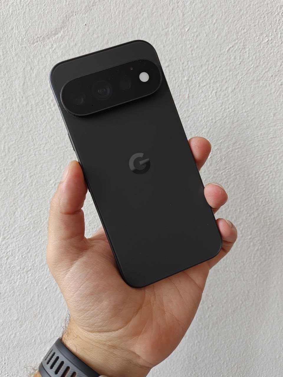 Retro del Google Pixel 11 Pro nero opaco tenuto in mano, con la barra delle fotocamere e il logo G
